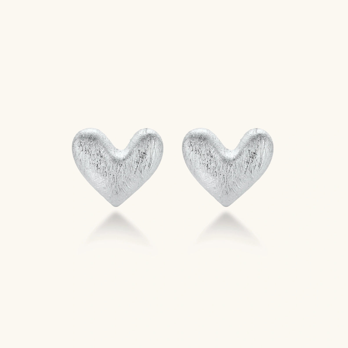 Pair of brushed platinum-plated 925 sterling silver puffy heart stud earrings on a cream background.