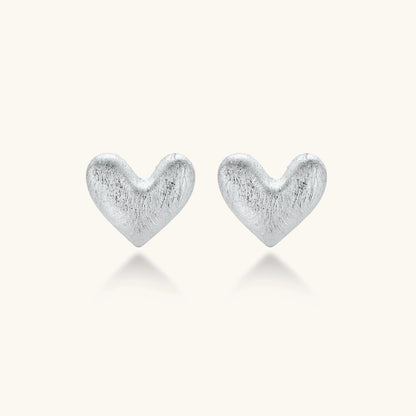 Pair of brushed platinum-plated 925 sterling silver puffy heart stud earrings on a cream background.