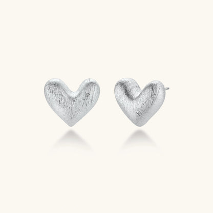 Pair of brushed platinum-plated 925 sterling silver puffy heart stud earrings on a cream background.
