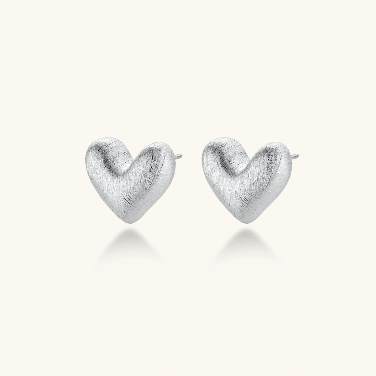 Pair of brushed platinum-plated 925 sterling silver puffy heart stud earrings on a cream background.