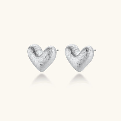 Pair of brushed platinum-plated 925 sterling silver puffy heart stud earrings on a cream background.